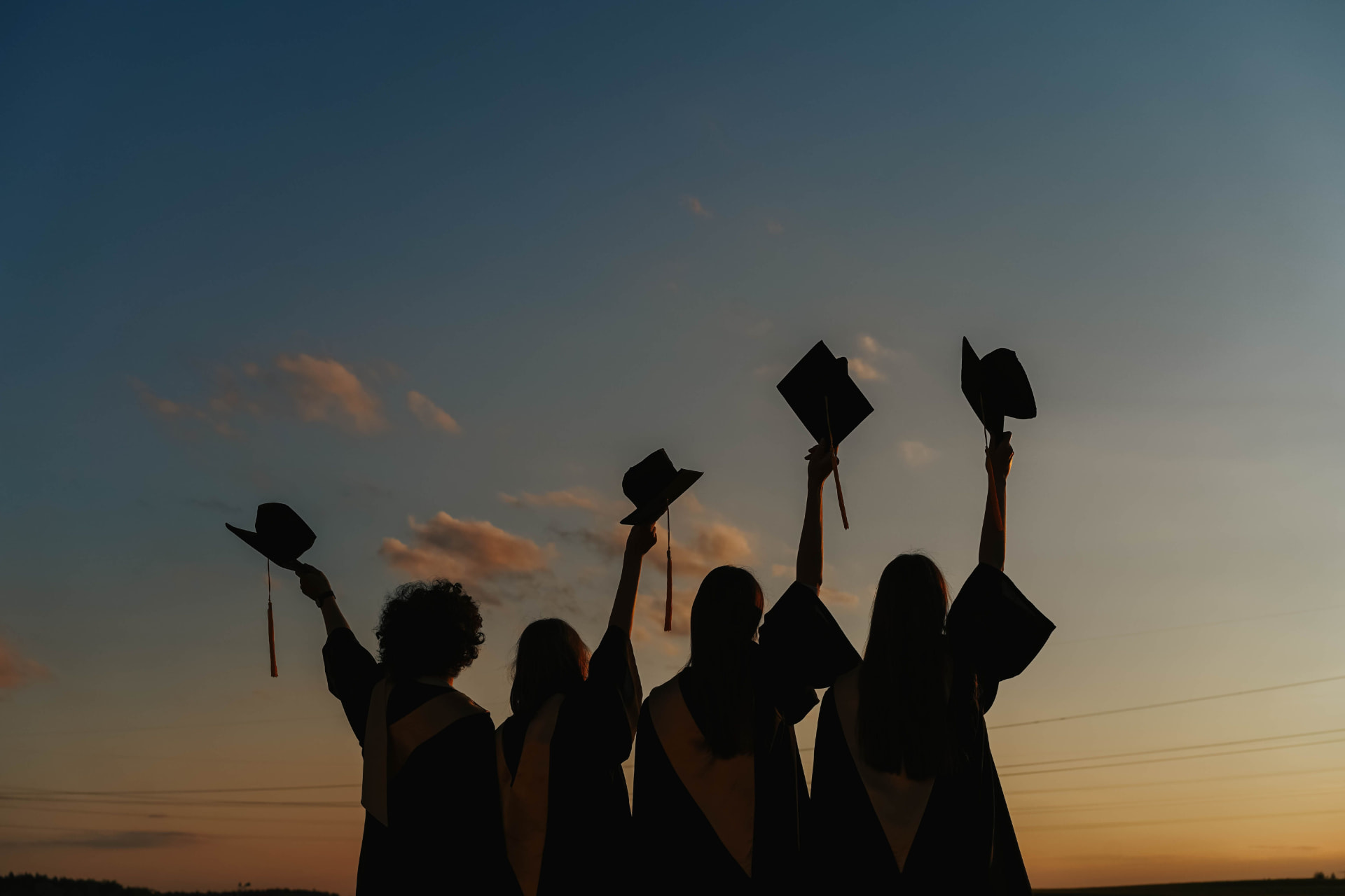 Graduates raising their caps at sunset